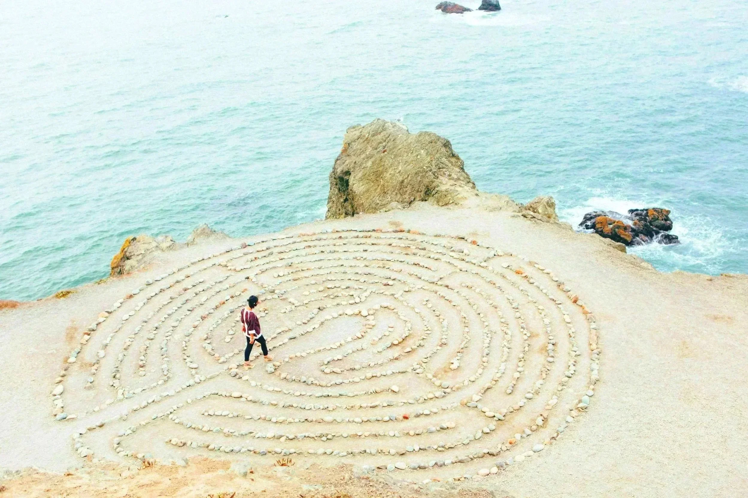 Person walking through a labyrinth made of stones on a cliff overlooking the ocean.