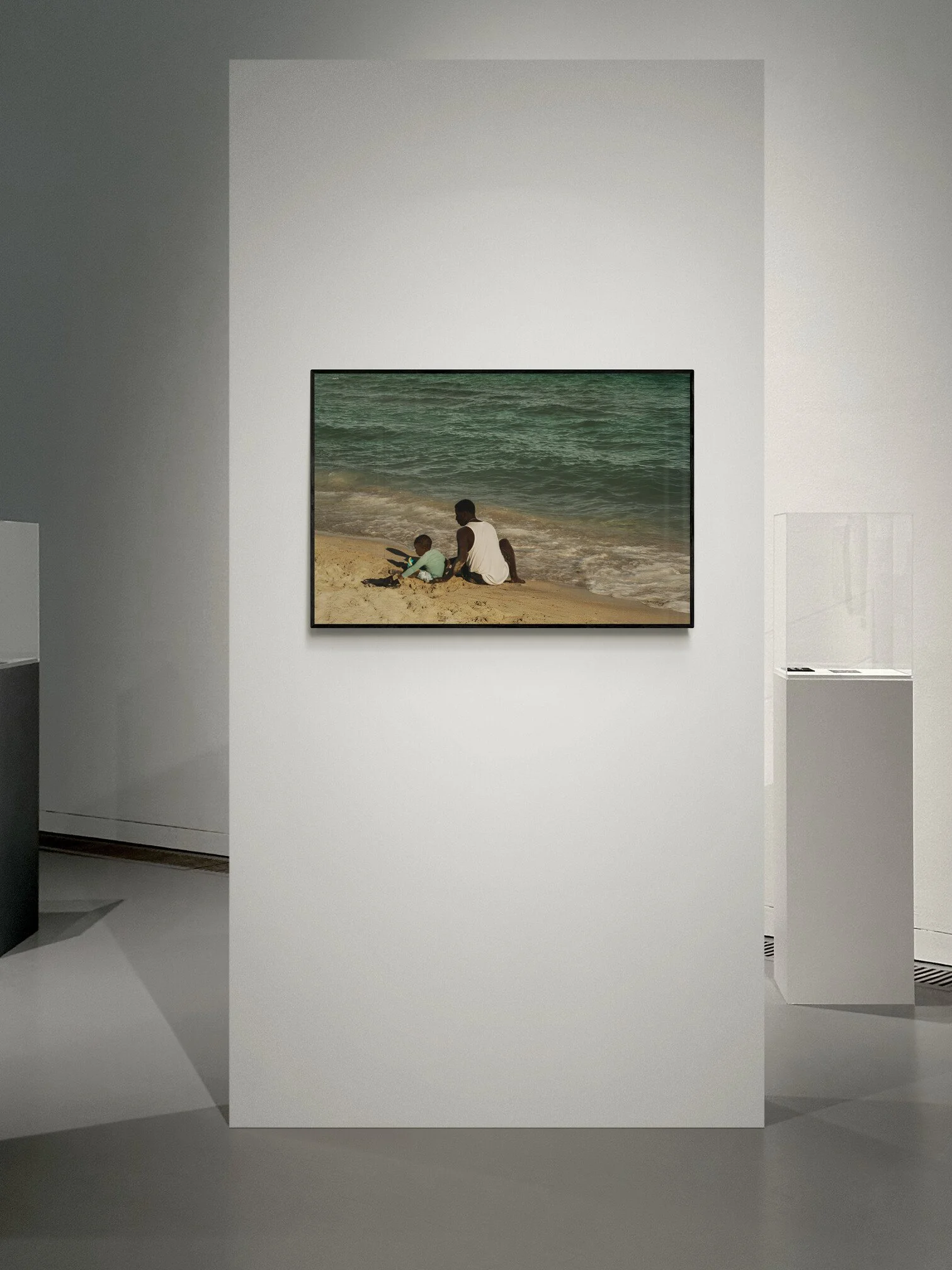 A framed photograph on a gallery wall depicting two people sitting on a beach near the ocean. Fine Art By Ton Gomes Photographer