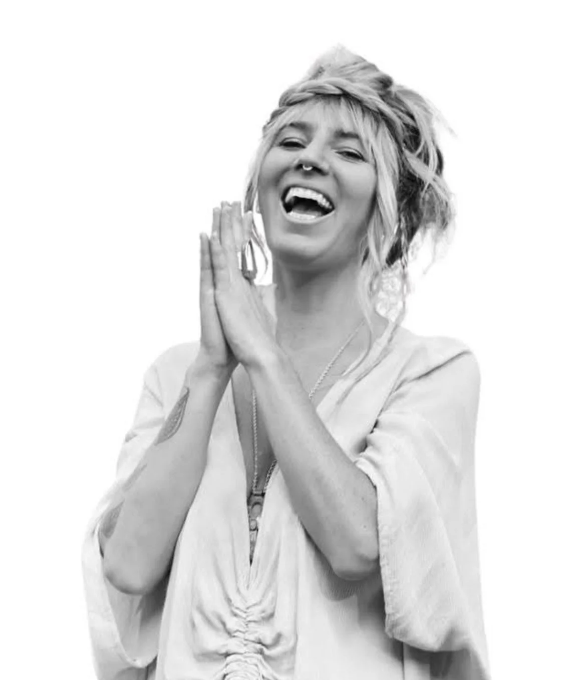 Black and white photo of a young woman with messy hair, smiling, with hands pressed together near her face, showing a joyful expression.