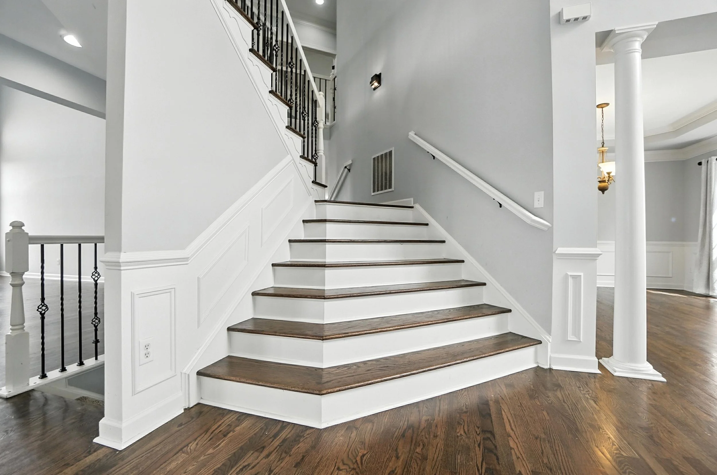 Interior view of a staircase with wooden steps, white risers, and a black handrail, in a home with hardwood floors and gray walls.