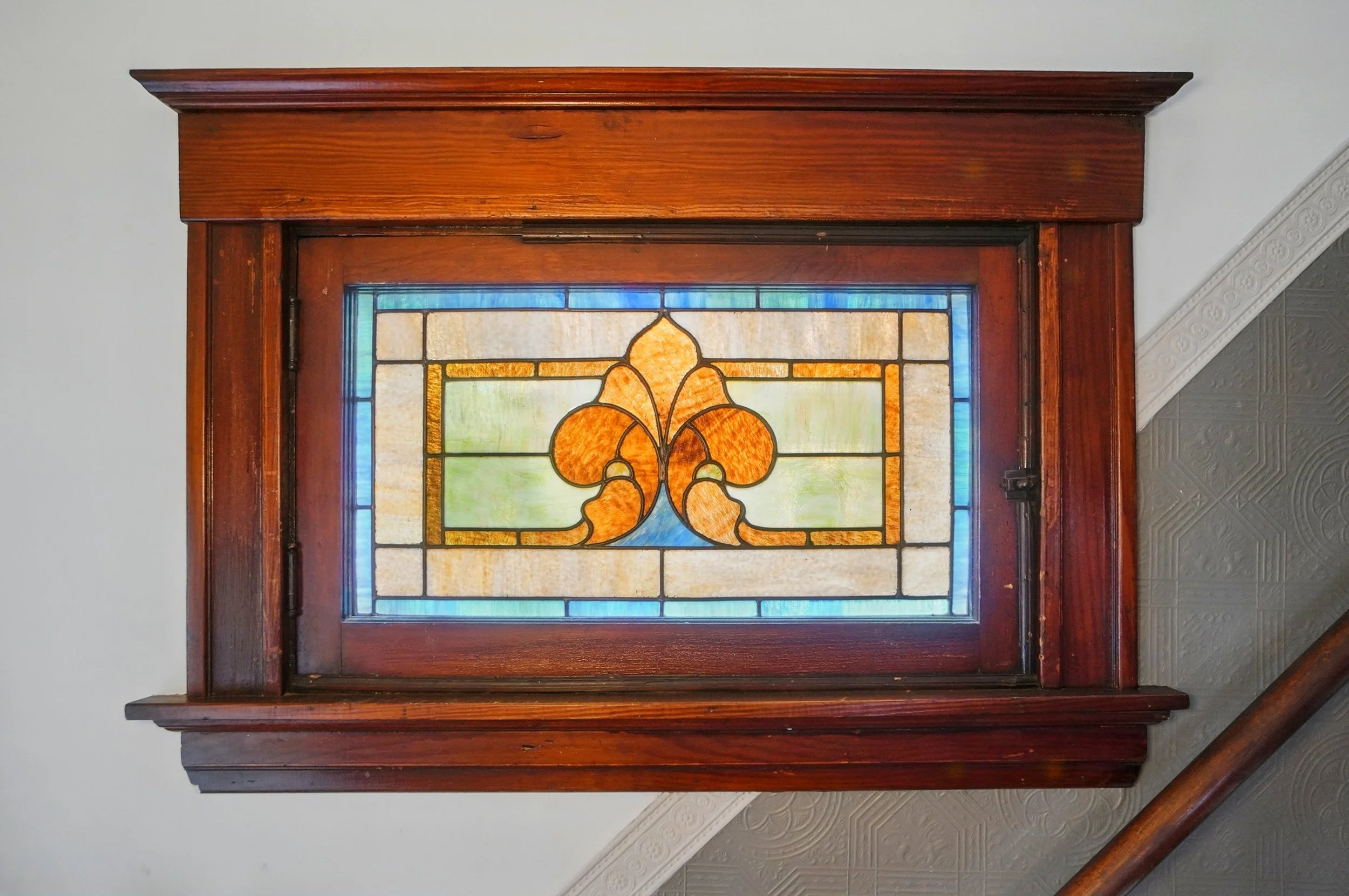 Decorative stained glass window with orange, yellow, and blue patterns in a wooden frame.