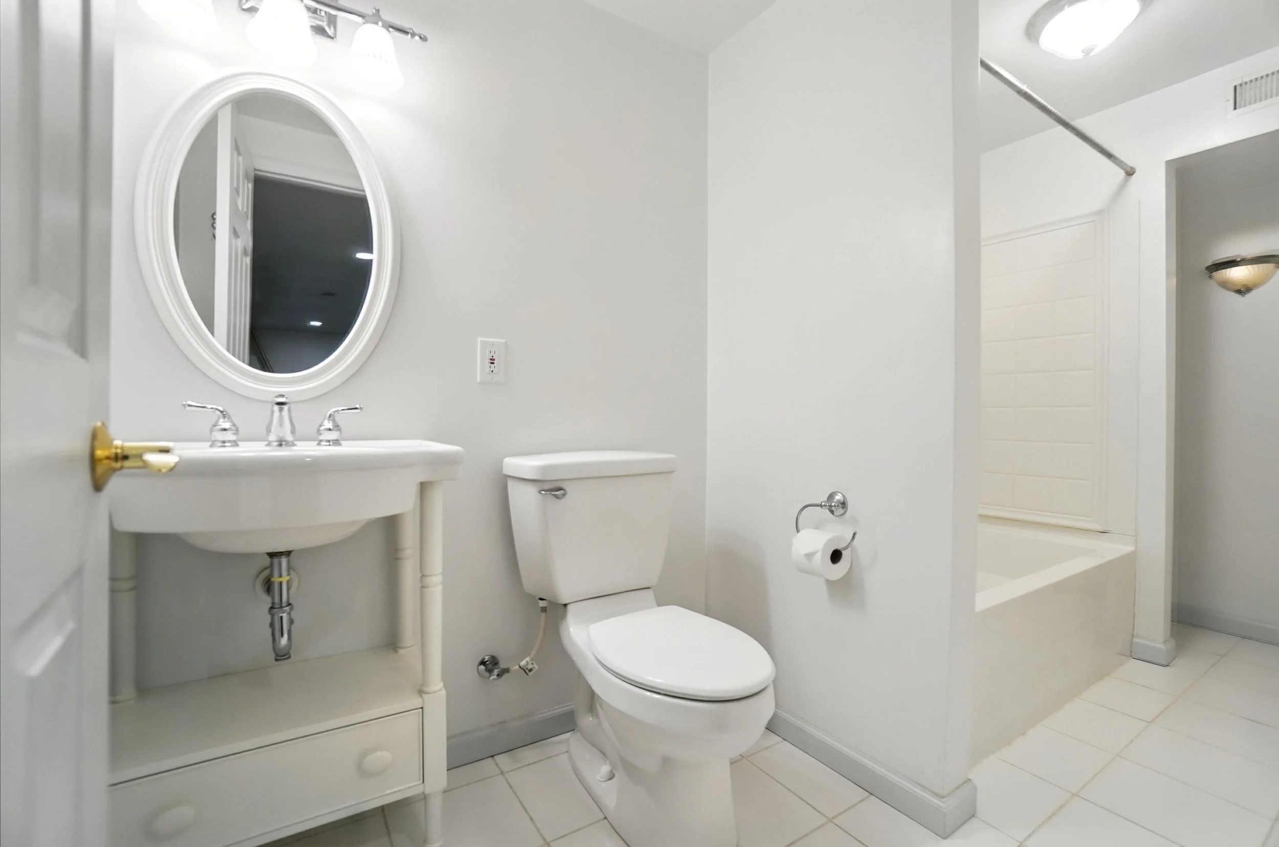 A small, white bathroom with a toilet, a small vanity with a mirror, a towel paper holder, and a bathtub with a shower curtain rod.