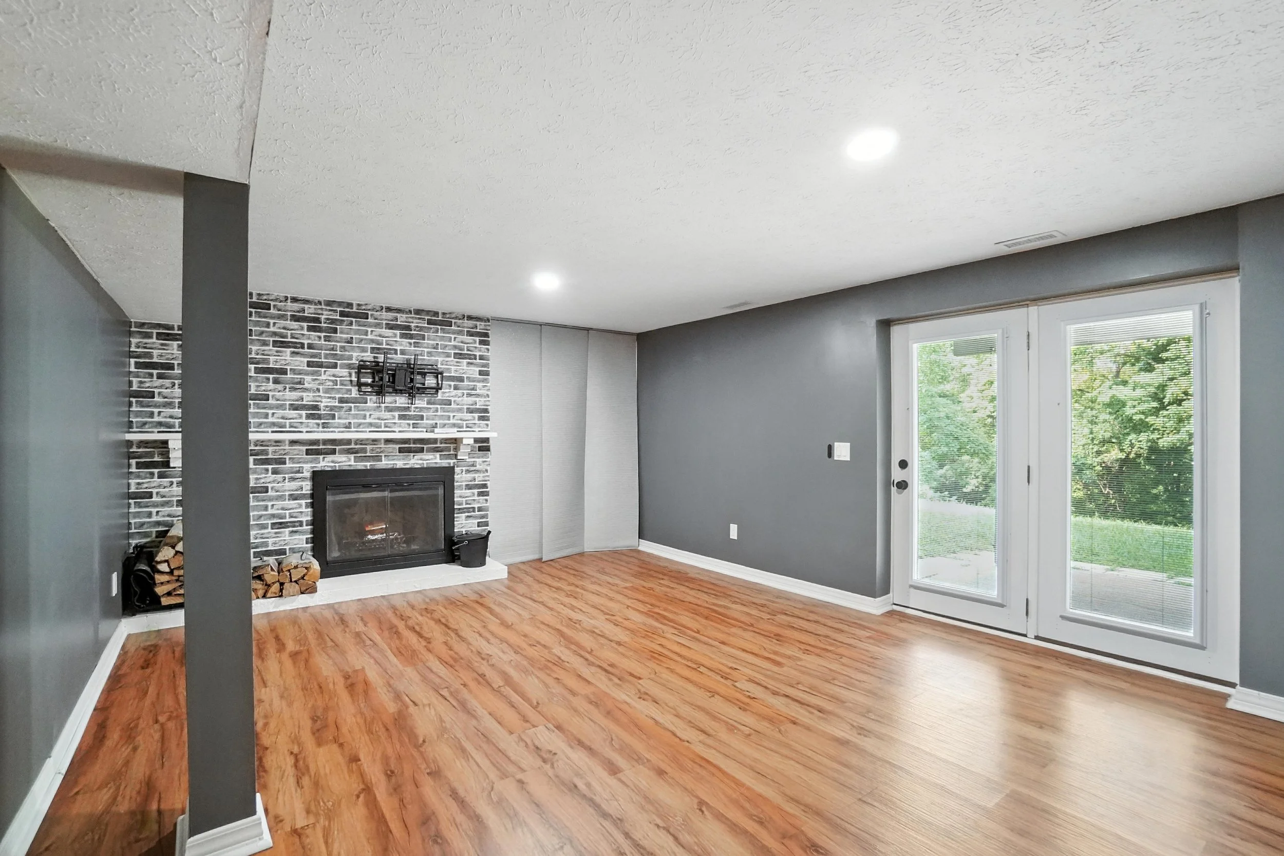 Empty living room with a fireplace, wood flooring, gray walls, and sliding glass doors leading to the outside.