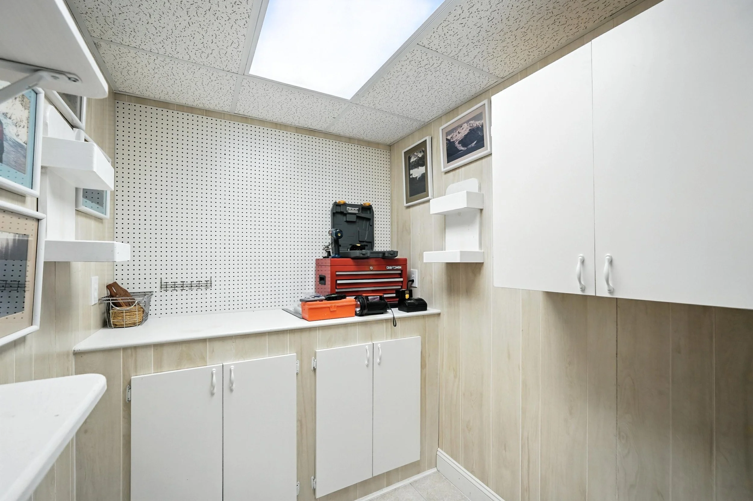 Empty workshop with white cabinets, pegboard wall, framed pictures, and a red toolbox.