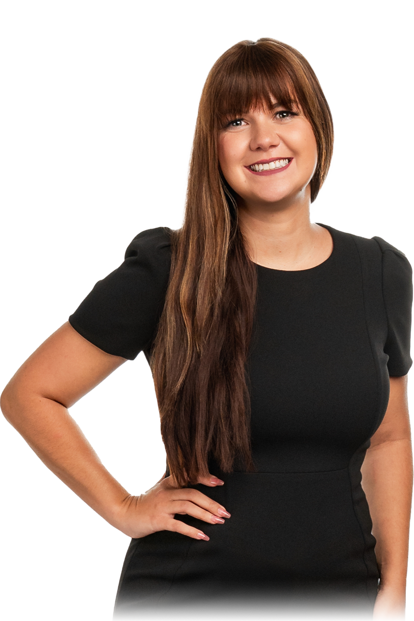 A woman with long brown hair and bangs, wearing a black short-sleeved dress, smiling and standing with her hand on her hip.