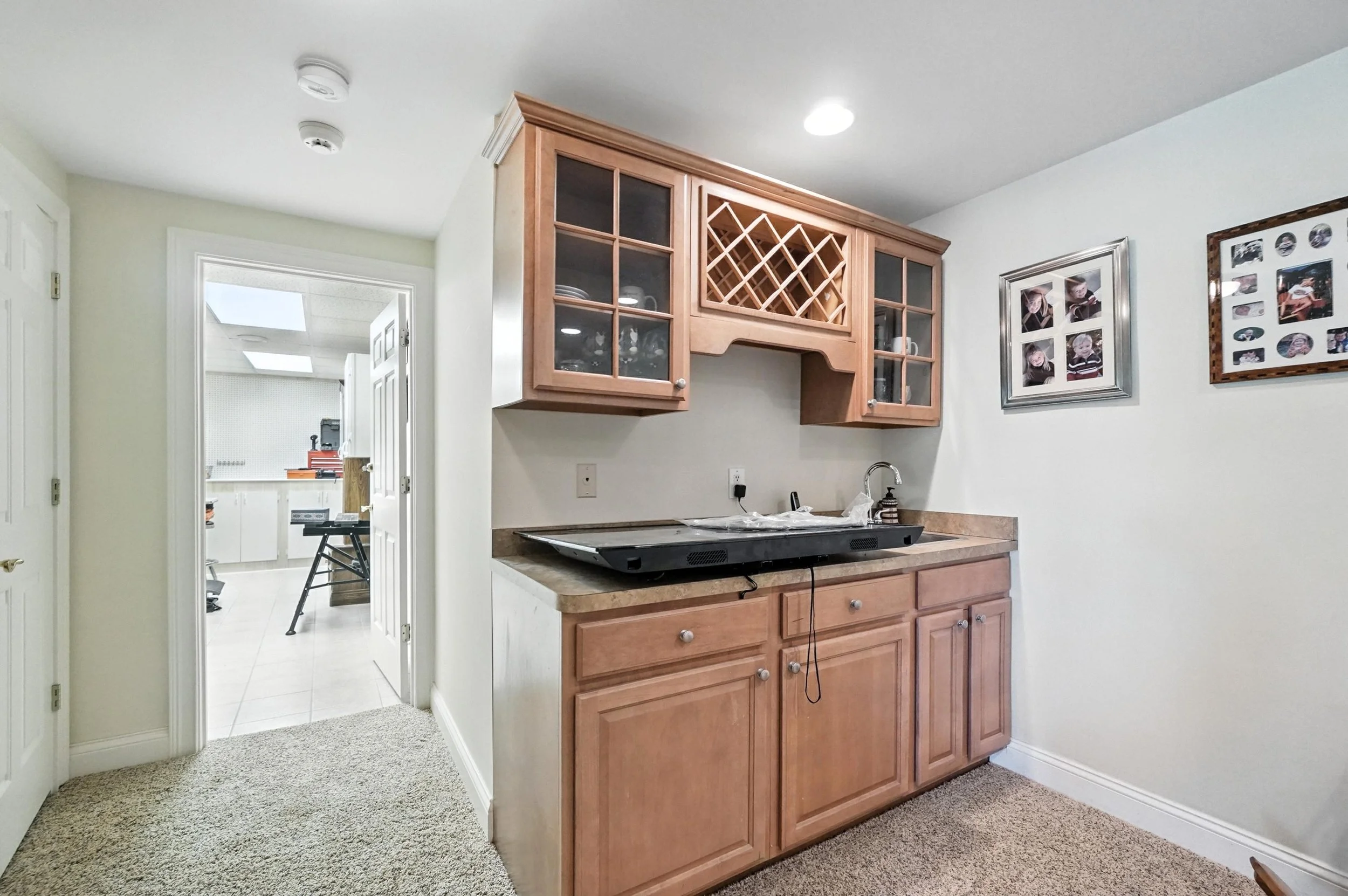 Kitchen area with wooden cabinets, a granite countertop, and a small sink. There are framed photos on the wall and a doorway to another room with a table and tools.