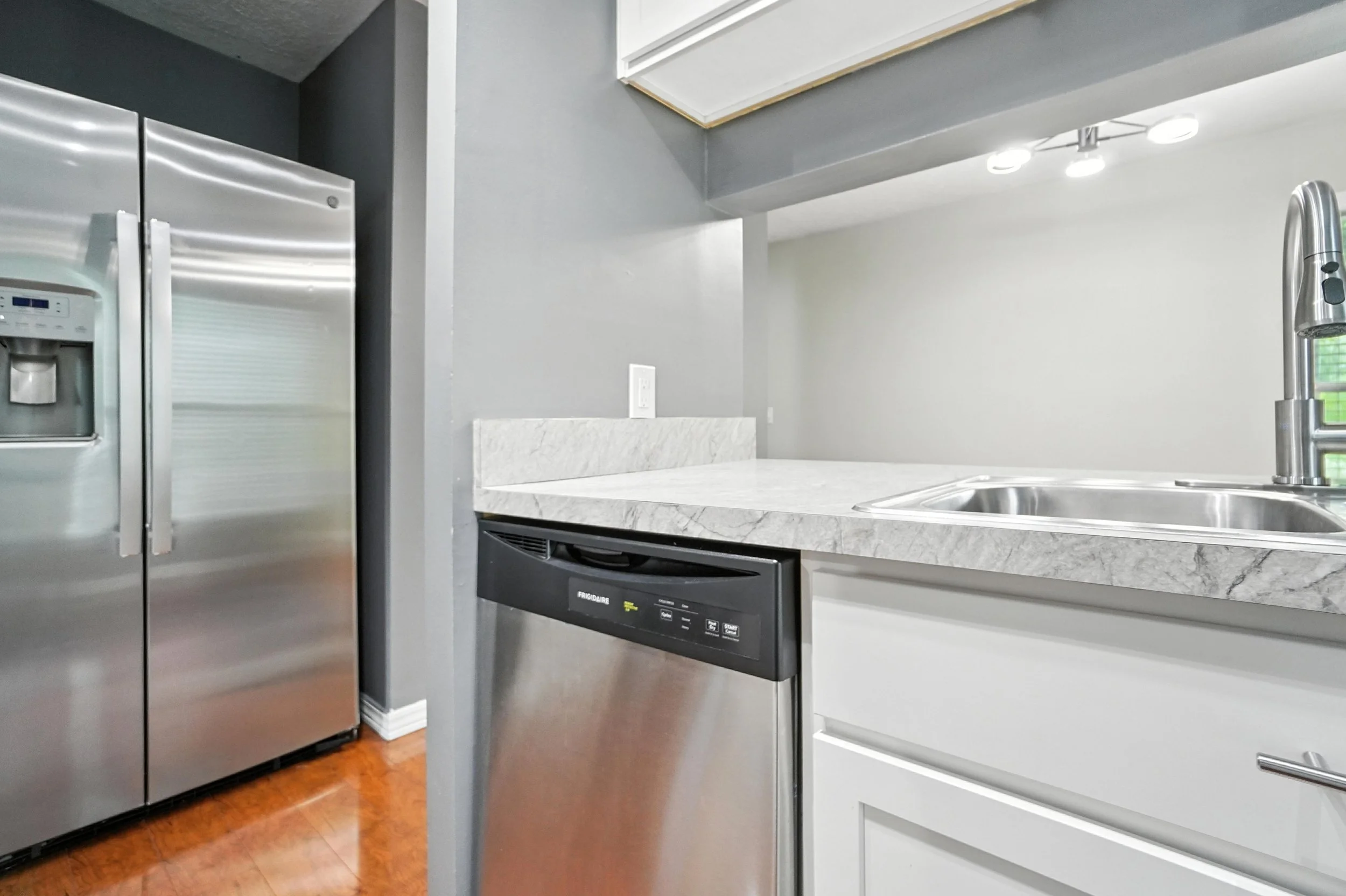 Modern kitchen with stainless steel refrigerator, dishwasher, and sink, gray walls, and a white marble countertop.
