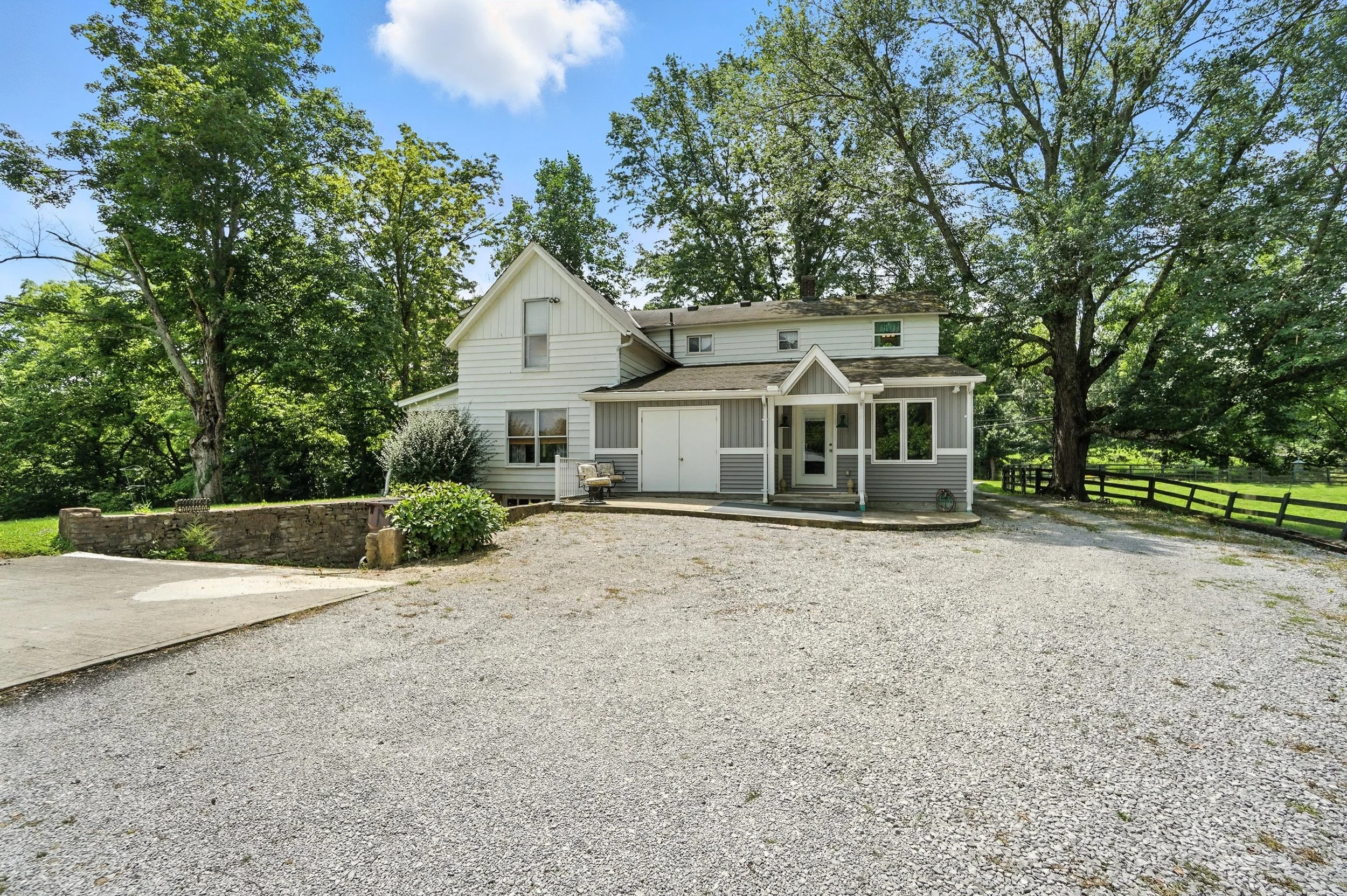 A white house with gray accents surrounded by green trees and a gravel driveway.
