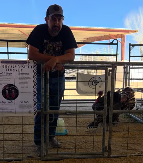Andre of Guerrero Heritage Ranch standing with Narragansett turkeys and a heritage turkey educational display at a community educational event.