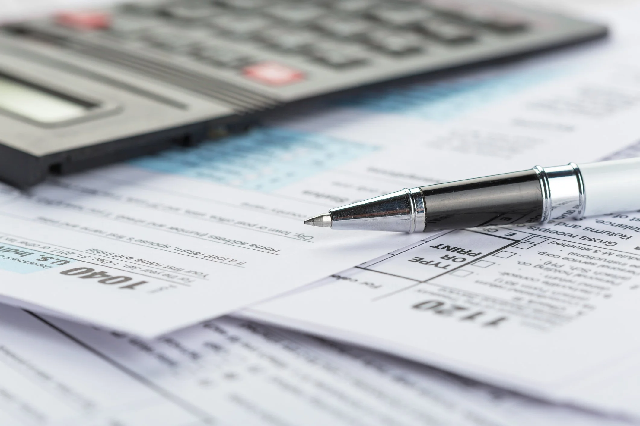 A silver pen resting on a set of papers and forms, with a calculator in the background.