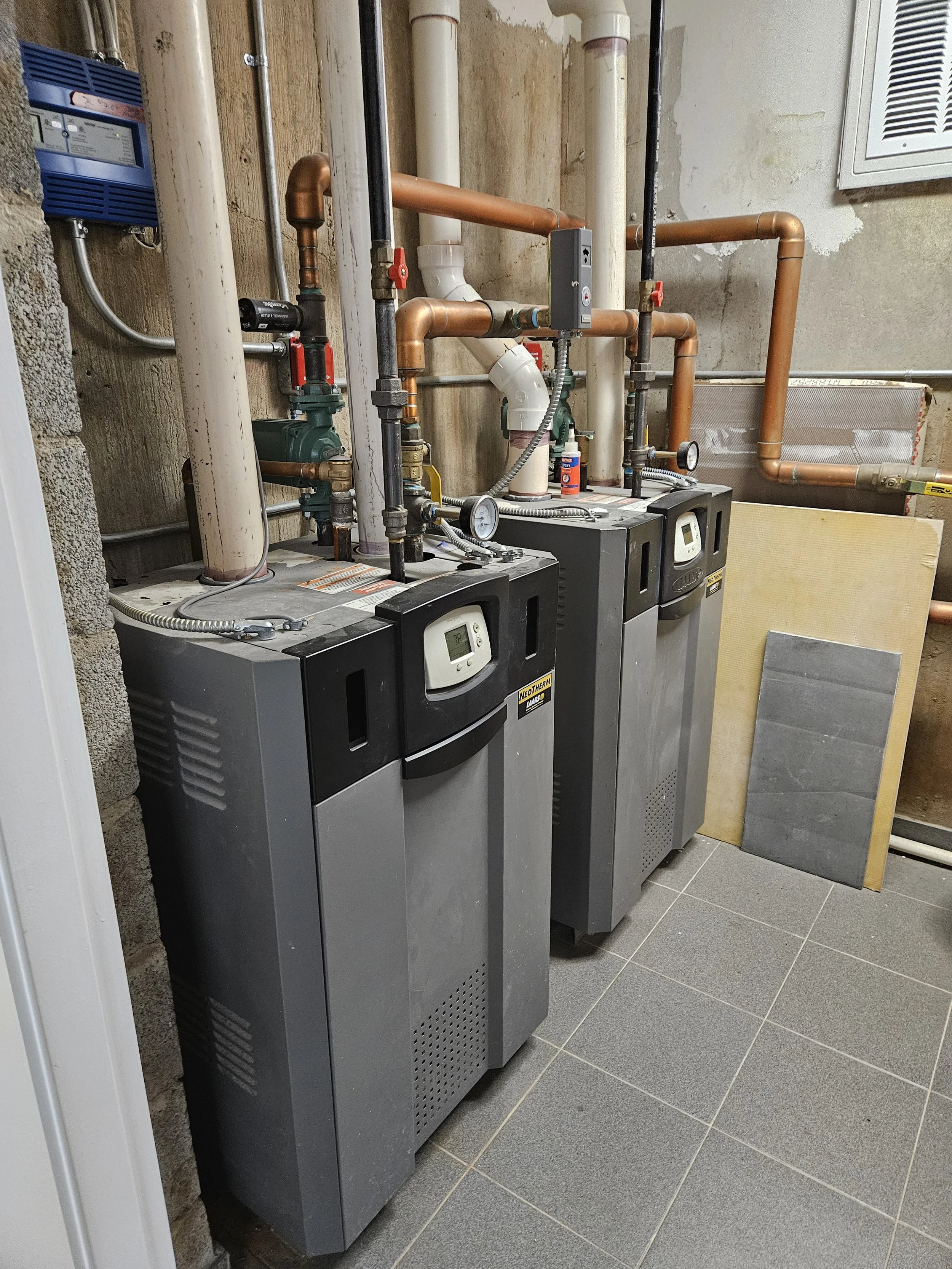 Two Laars residential high efficiency condensing boilers in a utility room with pipes and gauges, standing on tiled floor.