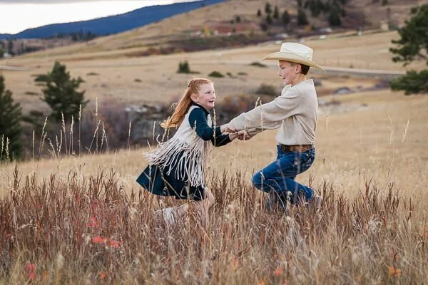 Girl & boy twirl each other around in meadow