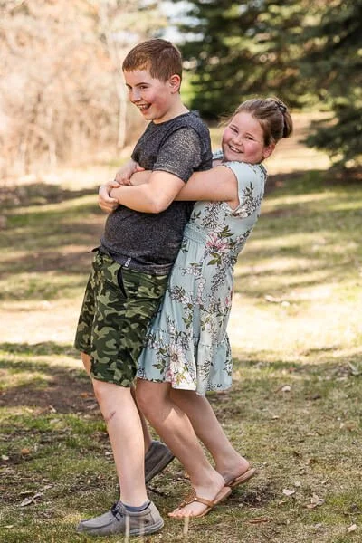 Girl tries to lift her older brother up from behind as they both laugh