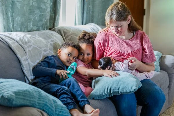 Mom nurses newborn while two older kids lean against her