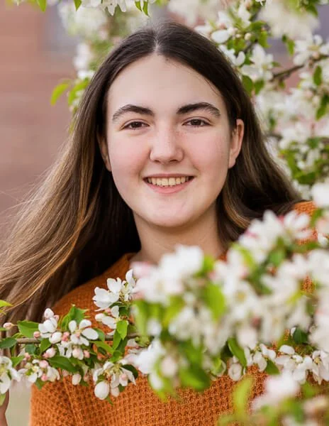 Teen girl peeks out from between white flowers