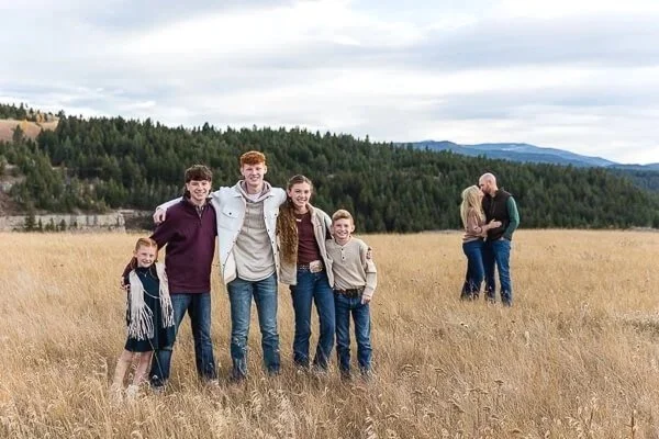 5 kids with their arms around each other's shoulders as parents kiss in the background at Sluice Boxes State Park
