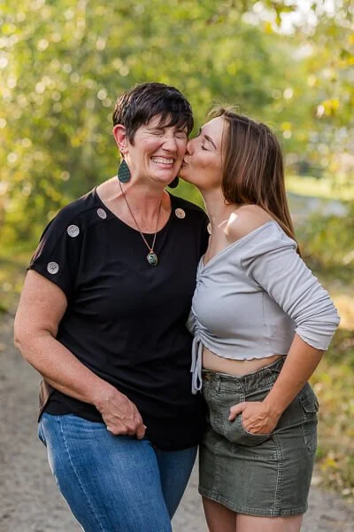 Mom scrunches up her face & smiles as teen daughter kisses her on the cheek