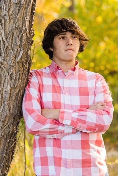 Teen boy in checkered shirt leans against tree