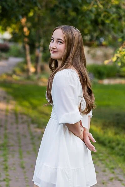 Teen girl in white dress looks over her shoulder 