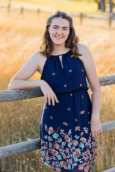 Teen girl in blue printed dress leans against picket fence