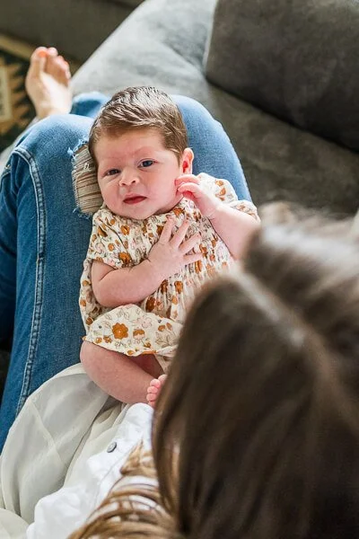 Newborn in cute floral print dresses gazes up from mom's lap