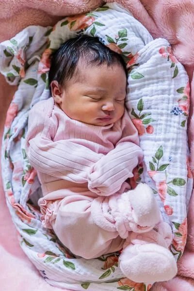 Sleeping baby girl curled up on rose-print blanket
