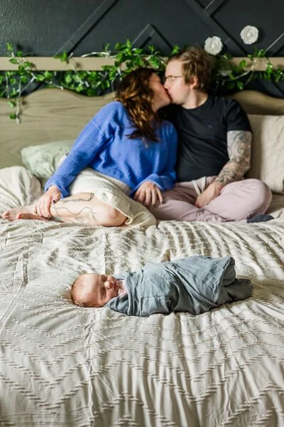 Parents kiss in the background with sleeping newborn in the foreground