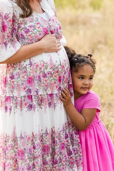 Little girl in pink dress snuggles against her mom's tummy

