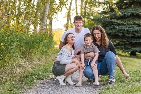 Three teens crouch down with their little brother and smile