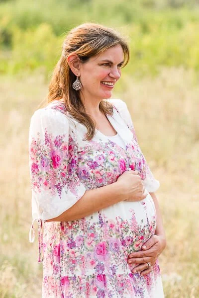 Pregnant woman cradles her baby bumps and smiles into the distance