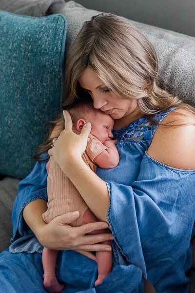 Mom in blue dress snuggles newborn against her chest