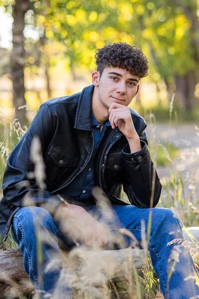 Senior boy with a pensive look sits on a fallen log