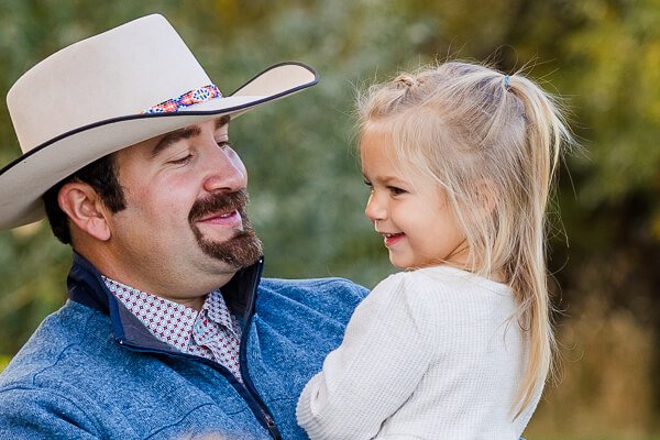 Dad wearing cowboy hat smiles at toddler daughter in his arms