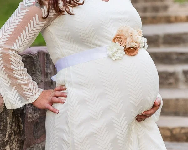 Expectant mom wearing cream colored dress cups her hand under belly