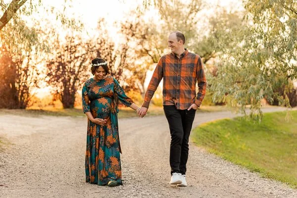 Pregnant woman cups her belly with one hand as she and husband walk holding hands
