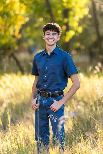 Teen boy in blue button down shirt standing in golden meadow