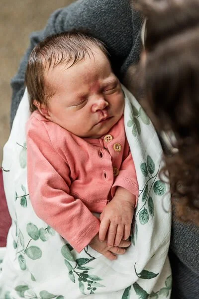 Baby in pink shirt wrapped in eucalyptus-leaf printed blanket