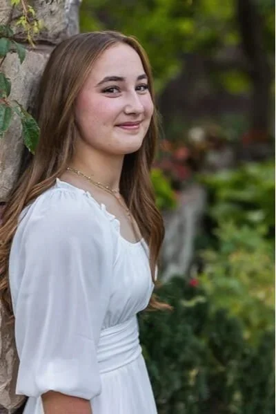 Girl in white dress leans against stone column