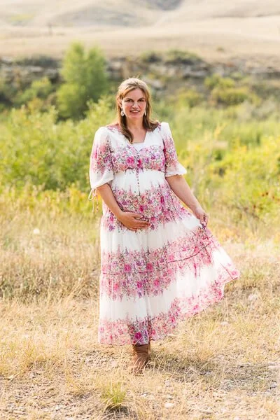 Pregnant woman wearing floral-print dress holds her skirt as she walks