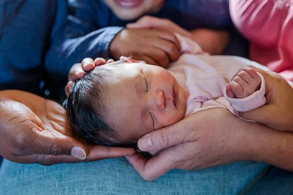 Newborn baby is surrounded by parents & siblings' hands