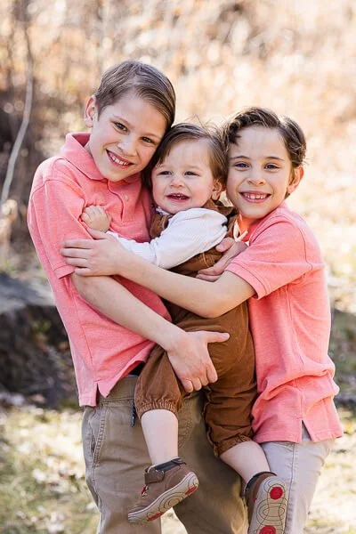 Two boys hug their toddler brother between them

