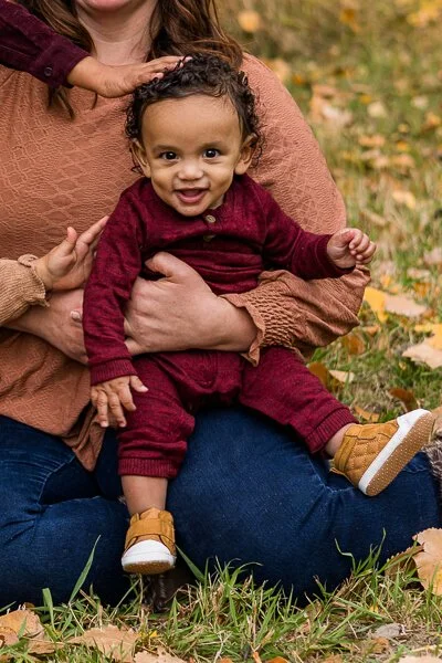 Baby smiles on mom's lap as his siblings reach out to touch him
