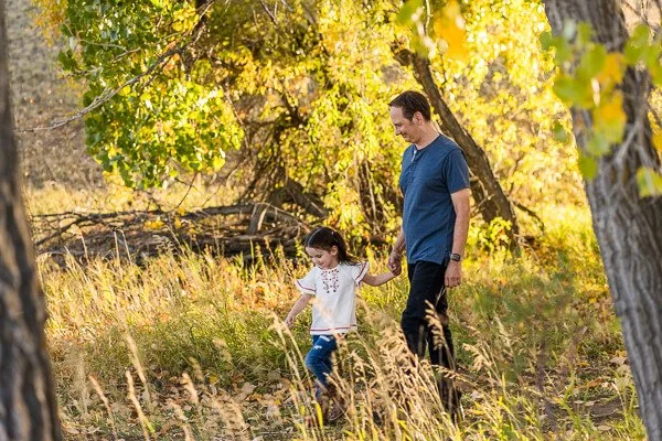 Little girl & father hold hands as they walk through the woods
