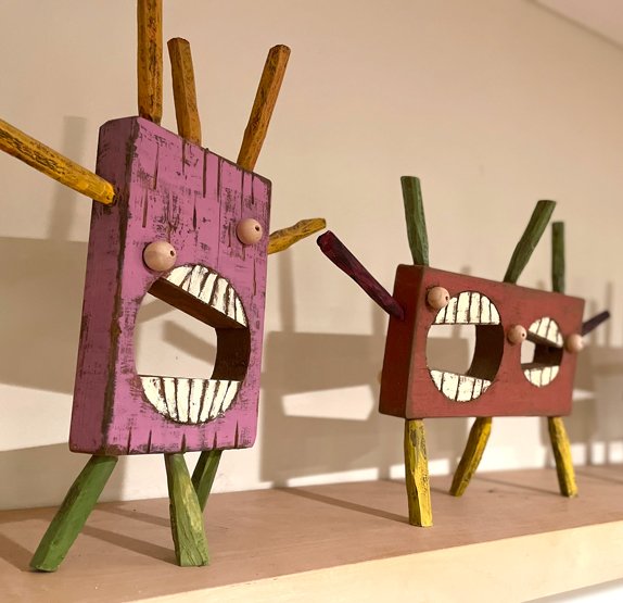 Colorful wooden sculptures with open mouths and stick-like limbs on display.