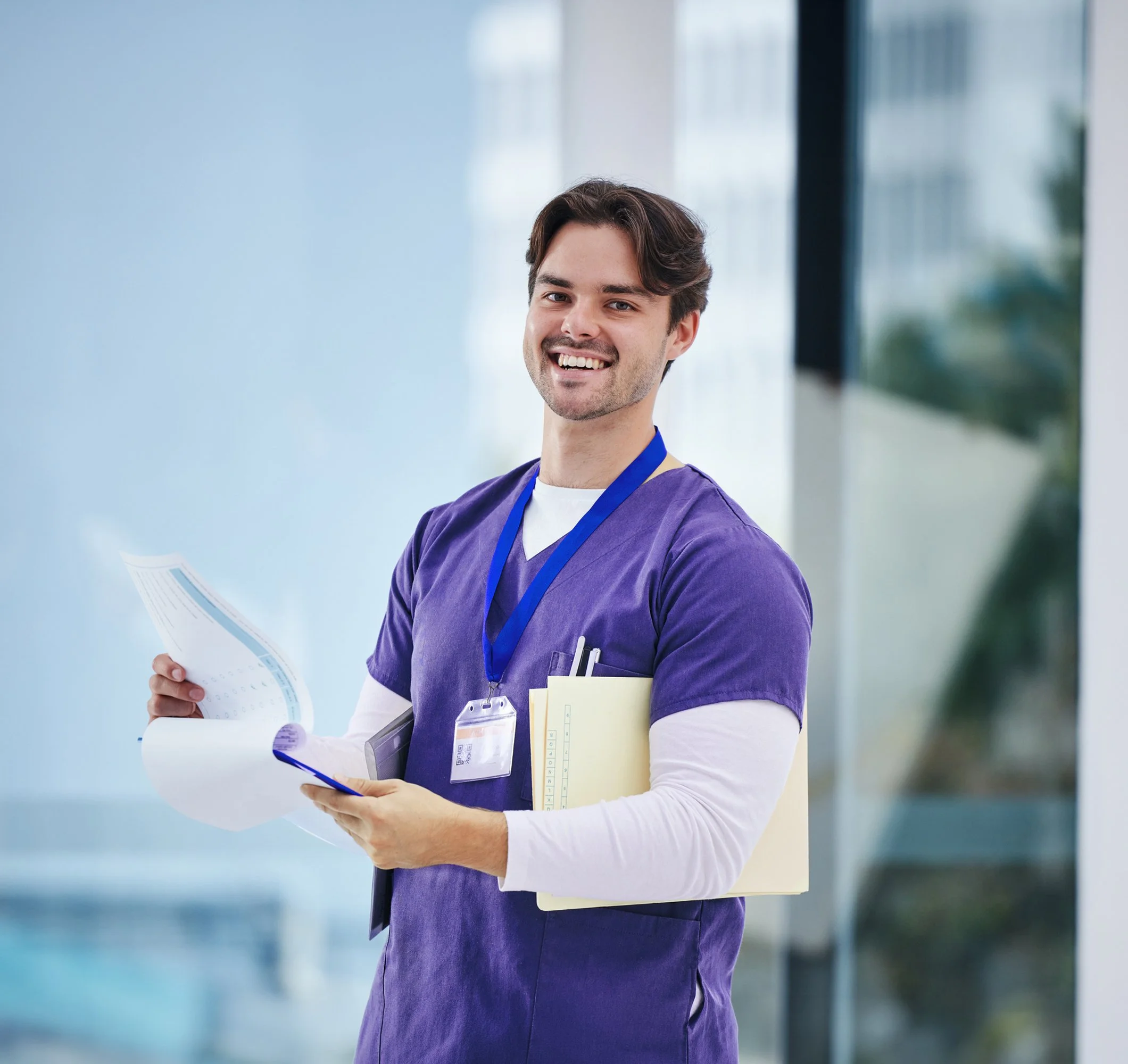 Smiling healthcare worker in purple scrubs holding paperwork and a folder