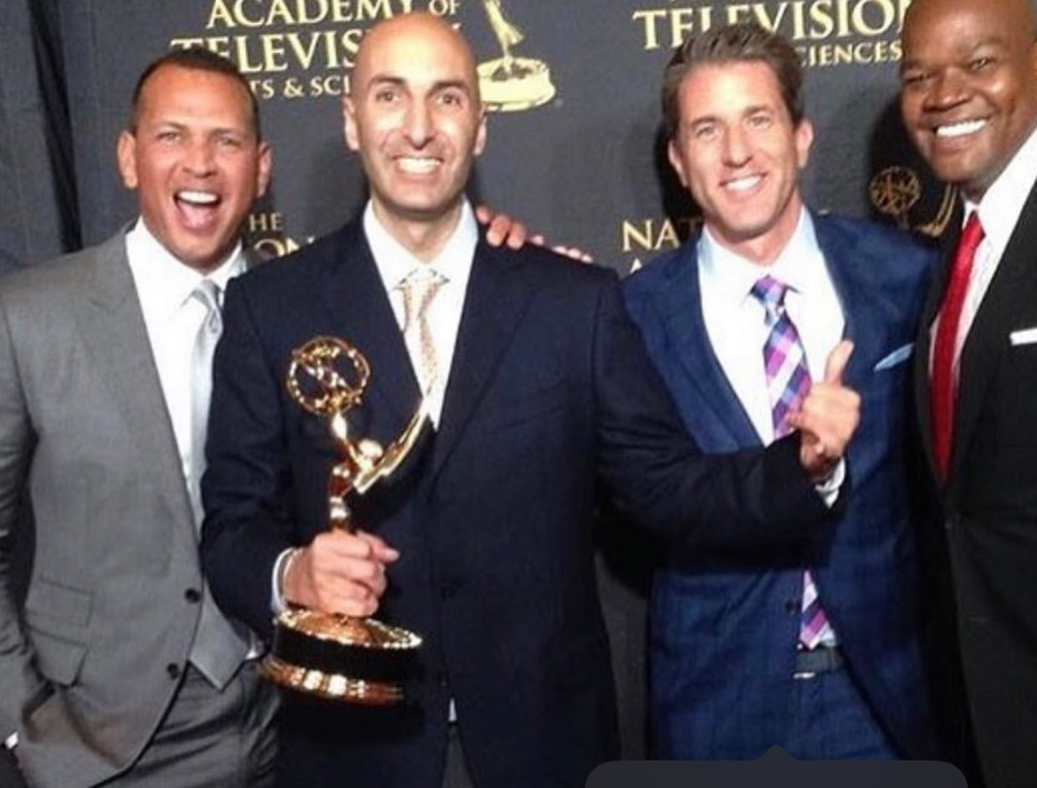 Holding an Emmy trophy. They are smiling and posing together in front of a black backdrop with gold text saying 'National Academy of Television Arts & Sciences'.