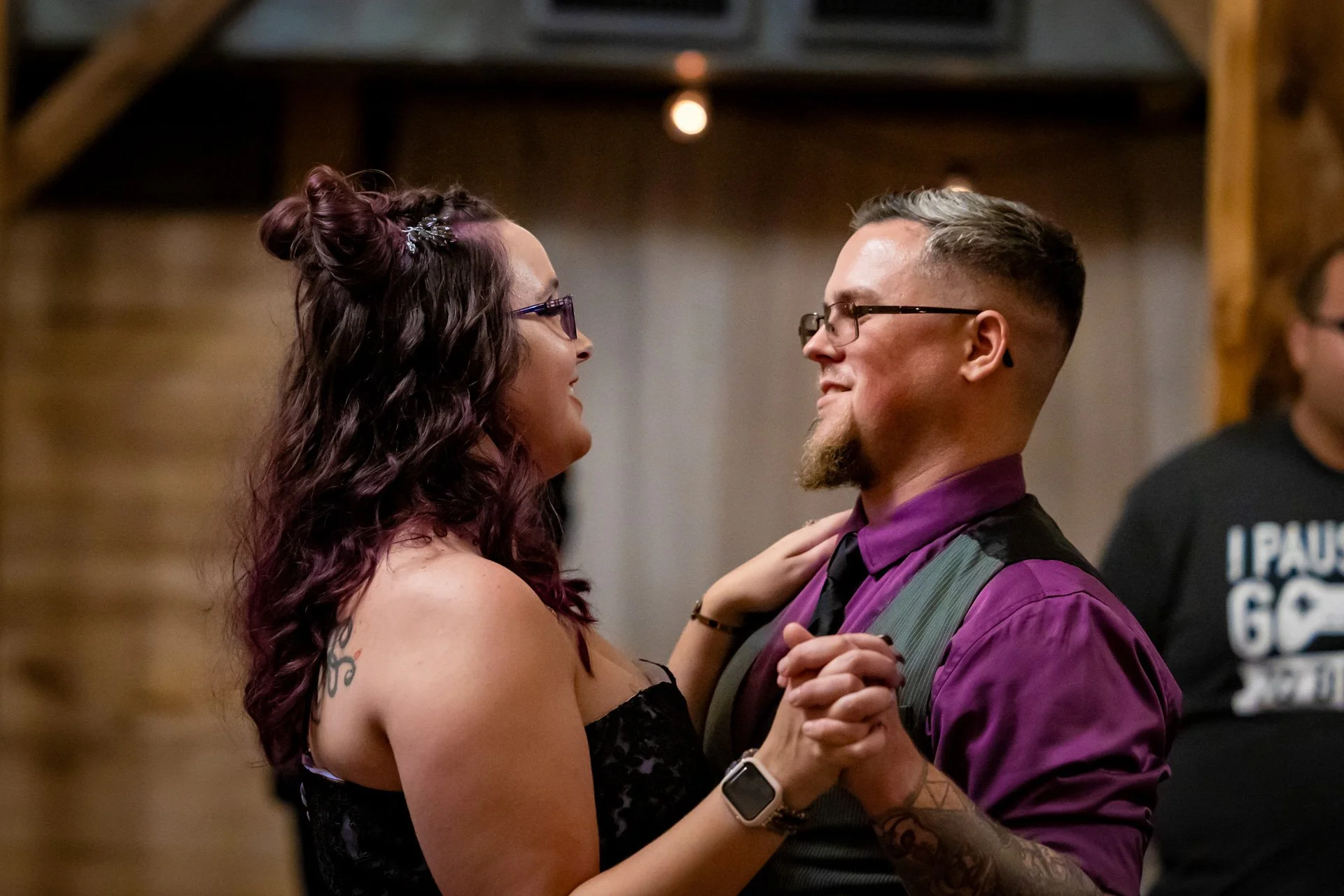 A couple dancing together, facing each other and smiling, in a warmly lit indoor setting.