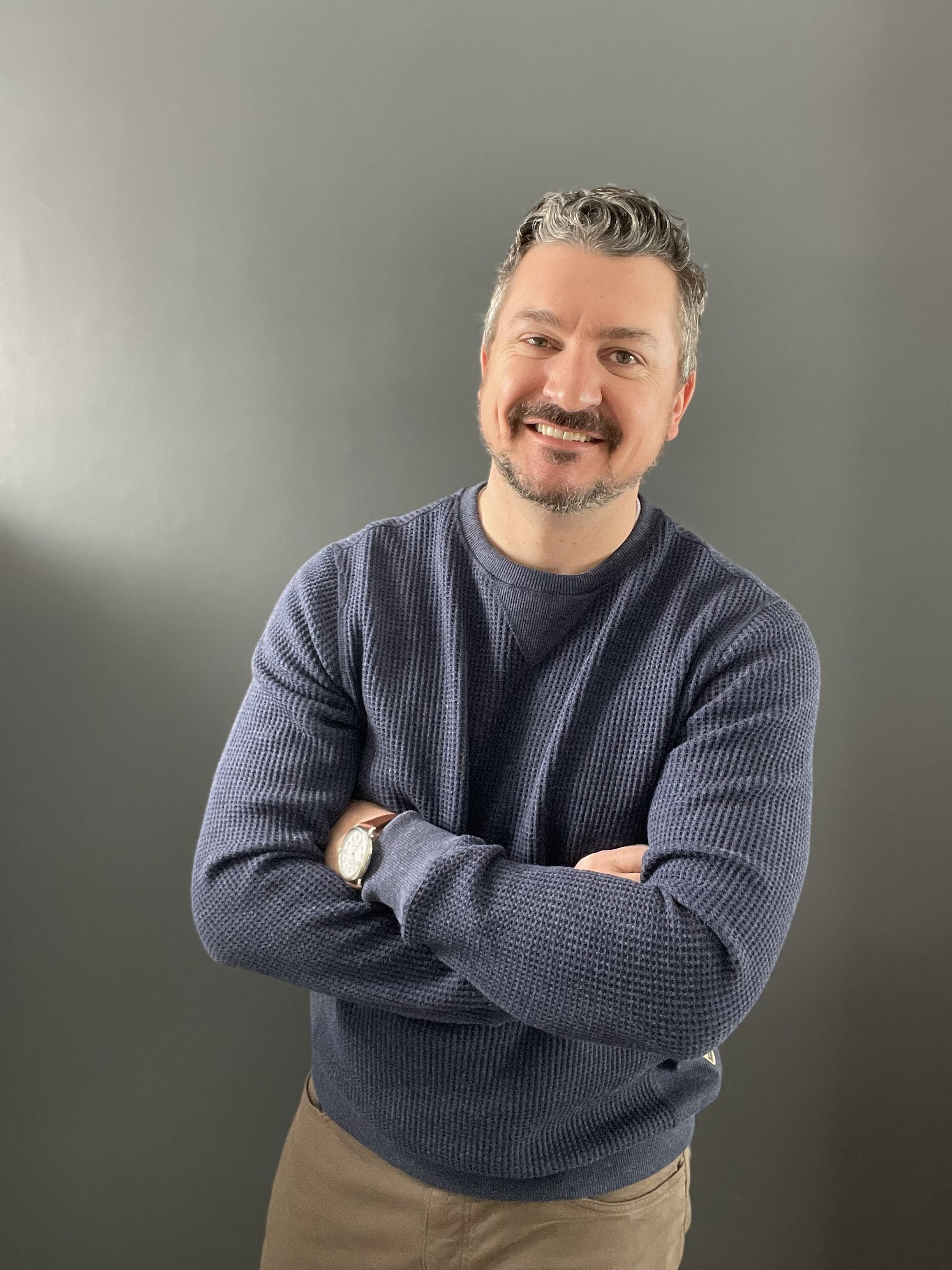 Man in blue sweater, arms crossed, smiling.