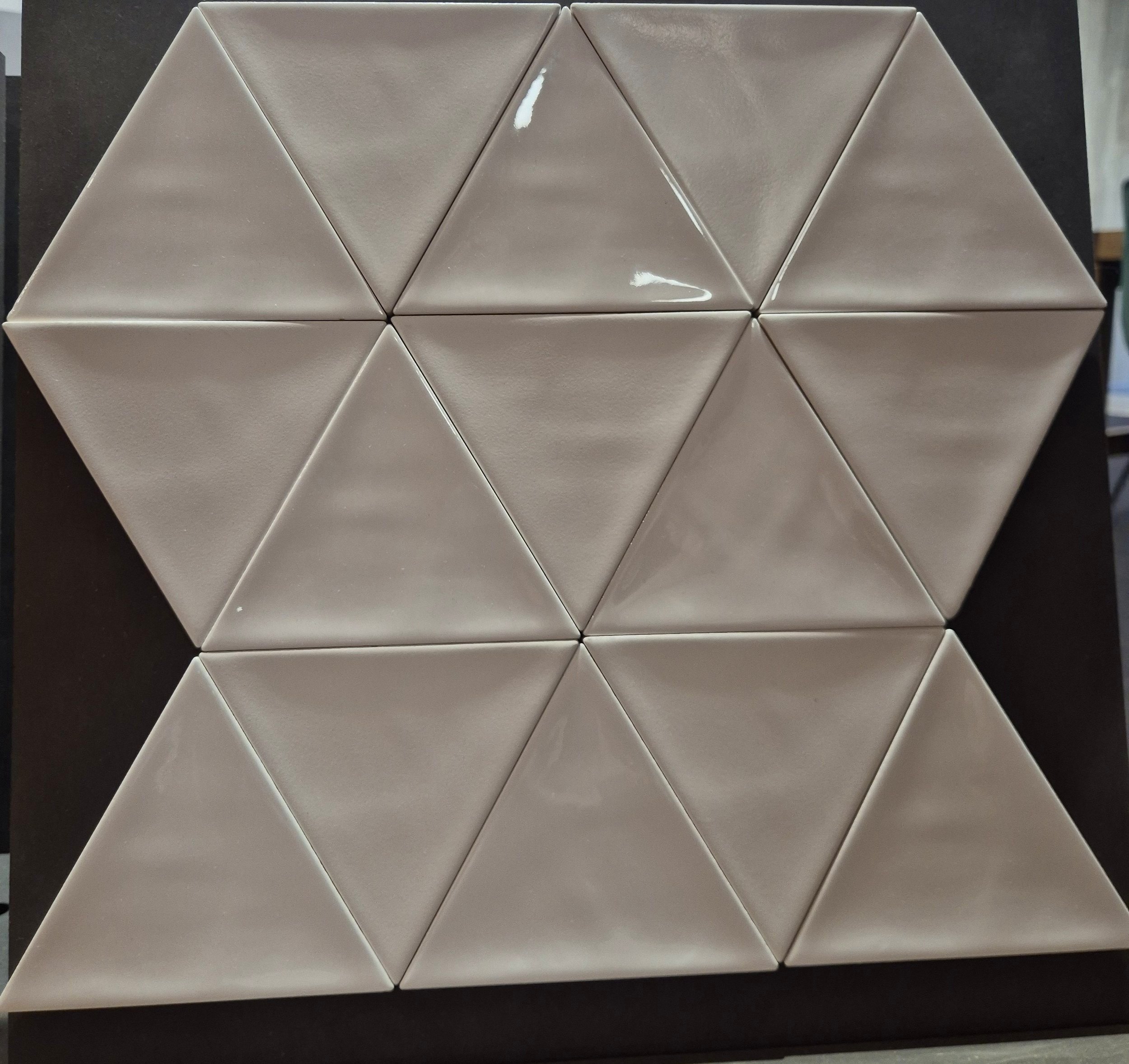 Beige driehoekige tegels gerangschikt in een geometrisch patroon op een donkere achtergrond.