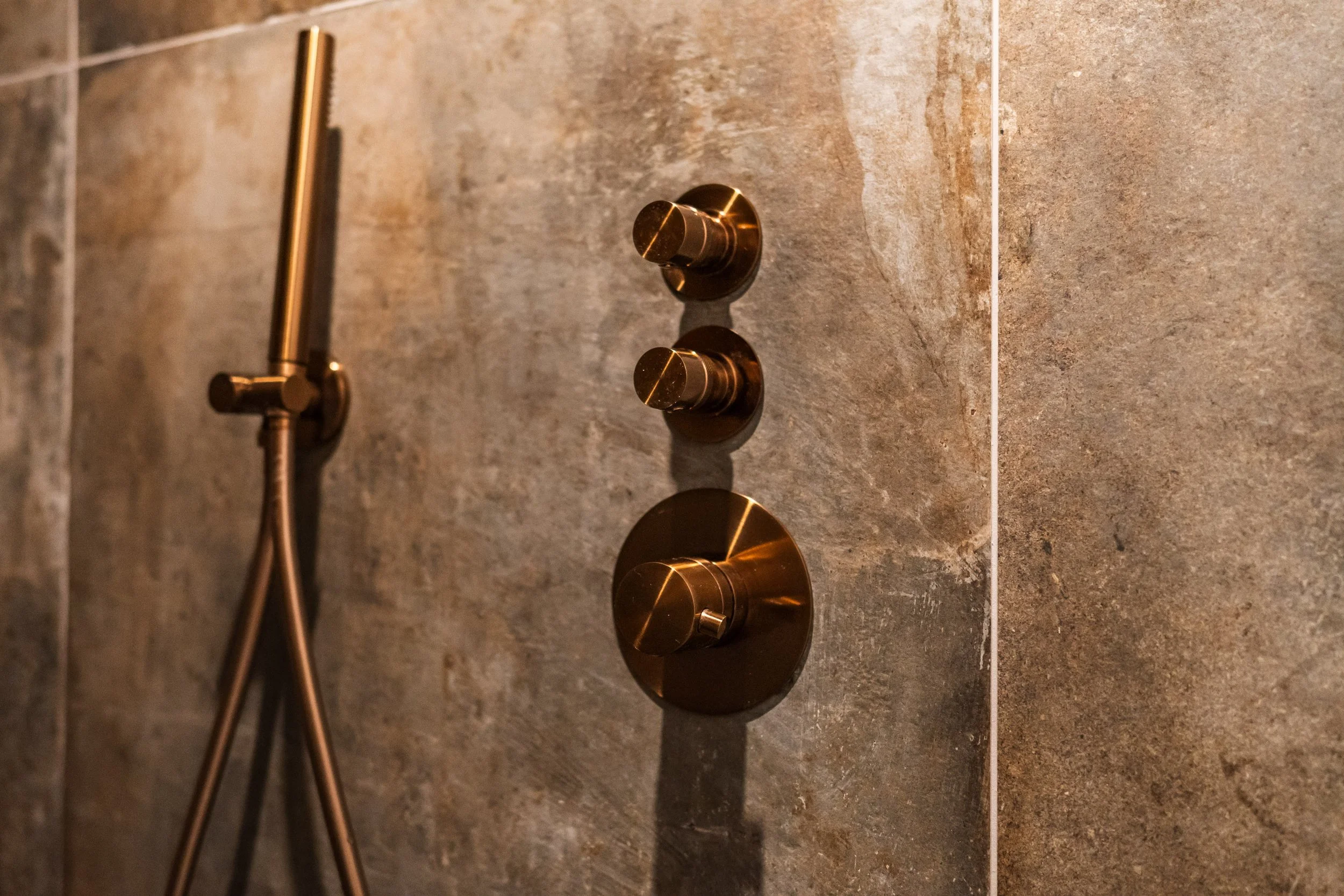 Doucheknoppen en handdouche in een badkamer met bruine tegels.